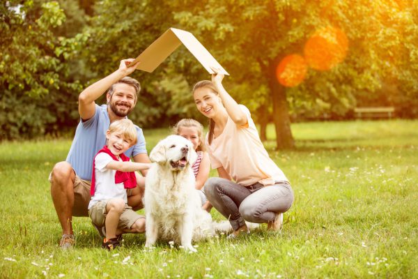 Familie mit Dach über dem Kopf im Garten als Symbol für Hausbau